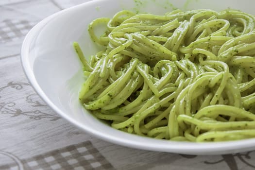 A close-up shot of spaghetti with traditional Genovese pesto sauce, served in a white bowl on a patterned tablecloth. Ideal for concepts of Italian cuisine, traditional recipes, and Mediterranean flavors.pasta, spaghetti, pesto, Italian food, dish, meal, cuisine, bowl, food, plate