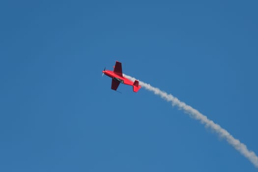 Red stunt aerobatic plane in inverted flight performing stunts in blue sky. Concept of speed, difficulty, precision, risk