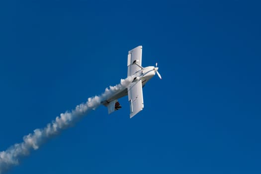 Stunt aerobatic plane in inverted flight performing stunts in blue sky with smoke trail. Concept of speed, difficulty, precision, risk, challenge