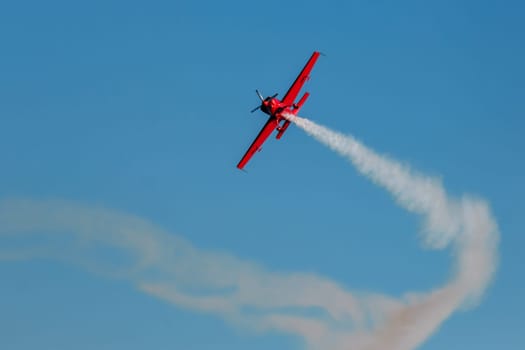 Red stunt aerobatic plane performing stunts in blue sky. Concept of speed, difficulty, precision, risk