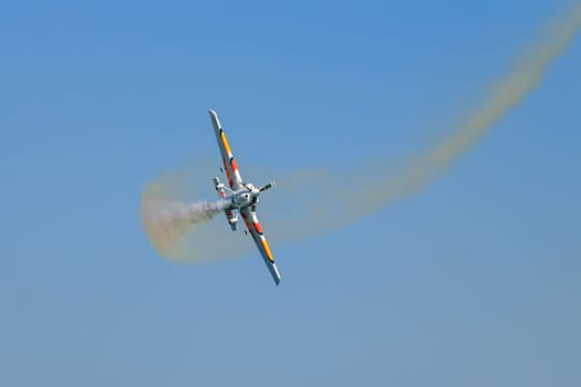 Stunt aerobatic plane performing stunts in blue sky with smoke trail. Concept of speed, difficulty, precision, risk, challenge
