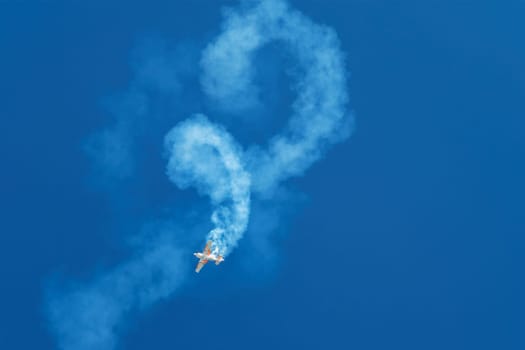 Stunt aerobatic plane performing stunts rolls loops in blue sky with smoke trail. Concept of speed, difficulty, precision, risk, challenge