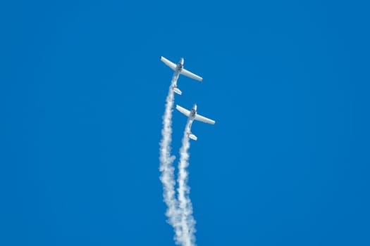 Stunt aerobatic plane performing stunts in blue sky with smoke trail. Concept of teamwork, collaboration, coordination, trust, precision, difficulty, challenge, speed, synergy