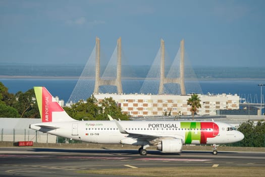 Lisbon, Portugal - September 2, 2023: TAP Air Portugal Airbus A321-251N passenger plane taxi on runway in Humberto Delgado Airport in Lisbon with Vasco da Gamma bridge in background