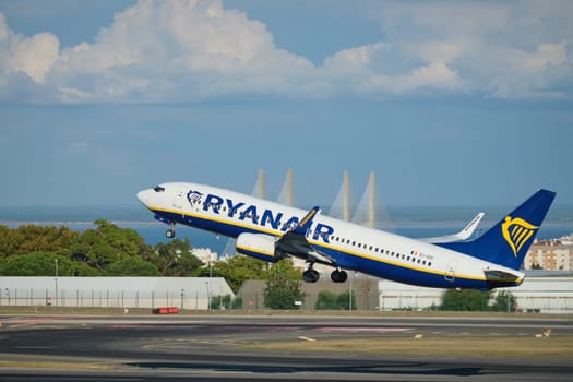 Lisbon, Portugal - September 2, 2023: Ryanair Boeing 737-8AS passenger plane take off in Humberto Delgado Airport in Lisbon with Vasco da Gamma bridge in background