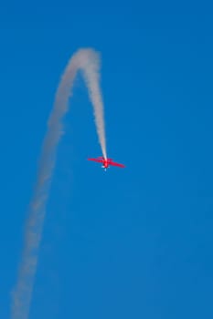 Red stunt aerobatic plane inverted flying loop performing stunts in blue sky. Concept of speed, difficulty, precision, risk