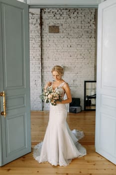 A stunning bride wearing a lace gown stands gracefully at an open doorway, holding a beautiful bouquet.