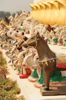 Many horse and elephant statues, porcelaine figurines, figures, ceramic sculptures are lined up in a row next to the statue of King Chao Anouvong in Vientiane, Laos 2023