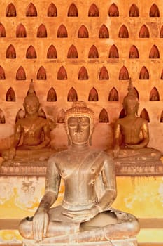 Three big buddha statues in front of a wall filled with many miniature buddha figurines in the cloister wall of Wat Si Saket, a buddhist temple in Vientiane, Laos 2023