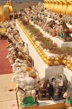 Many elephant and horse statues, porcelaine figurines, ceramic sculptures are lined up in a row next to the statue of King Chao Anouvong in Vientiane, Laos 2023