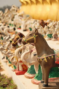 Many horse and elephant statues, porcelaine figurines, ceramic sculptures are lined up in a row next to the statue of King Chao Anouvong in Vientiane, Laos 2023