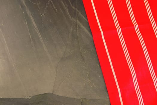 Red white striped tablecloth on massive slate plate or black stone background texture. Template for design menu card and blackboard. Copy space. Top view.
