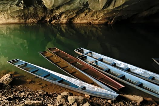 A few long boats, some of them partly submerged, sunken at the entrance of Kong Lor Cave, a tourist attraction on the Thakhek Motorbike Loop, Laos 2023