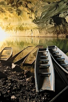A few long boats, some partly submerged, sunken at the entrance of Kong Lor Cave, a tourist attraction on the Thakhek Motorbike Loop, Laos 2023