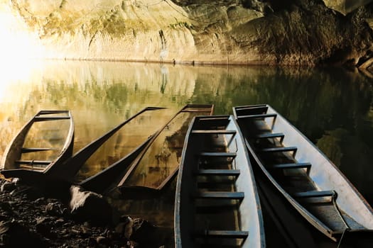 A few long boats, some of them submerged, sunken at the entrance of Kong Lor Cave, a tourist attraction on the Thakhek Motorbike Loop, Laos 2023