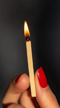 A close-up of a hand with red nails holding a lit matchstick against a dark background, evoking warmth, ignition, and contrast.