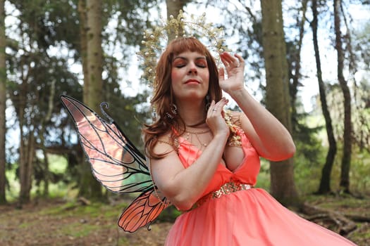 A beautiful elf with a crown and wings sits in a forest