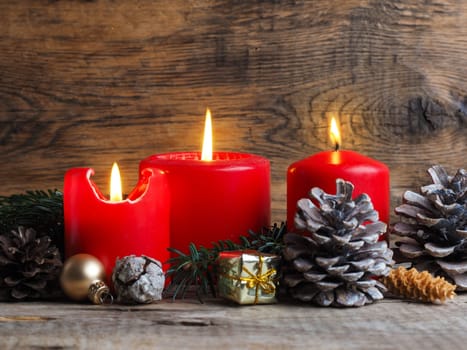 Red Advent candles on a rustic wooden background, third candle is burning, Christmas concept background