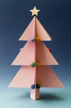 A small pink paper Christmas tree stands against a blue background, adorned with colorful ornaments and a star atop its peak.