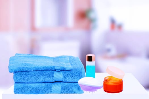 Table top on towels background. Closeup of fresh soft terry bath towels with massage brush, cosmetic cream and soap bottle over blurred bathroom background. Space.