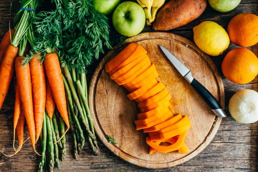 Top view of healthy bio food ingredients for smoothie preparation on wooden table. Organic superfood groceries cooking from above. Colorful fruits and vegetables in kitchen background. Butternut squash, carrots, sweet potato, oranges, apples, carrots and asparagus on cutting board overhead.