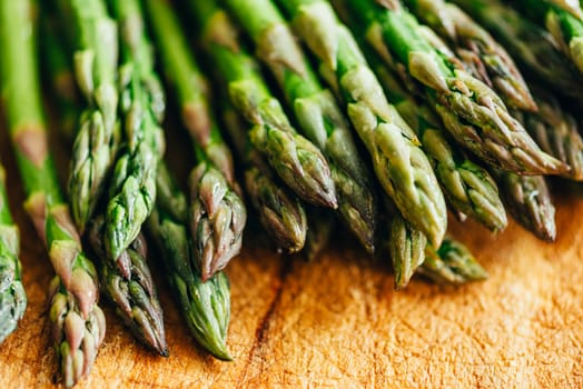 Closeup of fresh green asparagus on vintage wooden table. Cooking vegetarian food with organic ingredient on rustic board. Healthy vegetable salad recipe preparation.