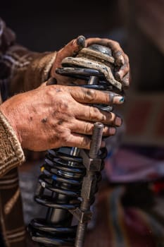 Dirty and calloused hands of a mechanic assembling compressed coil spring during DIY car repairs. Closeup.