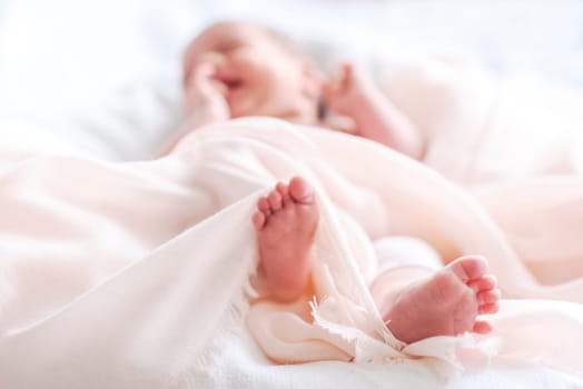 Cute newborn baby in white soft blanket after bath. Closeup of infant foot and blur pastel background. Child skincare and health care.