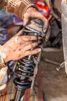 Dirty and calloused hands of a mechanic assembling compressed coil spring during DIY car repairs. Closeup.