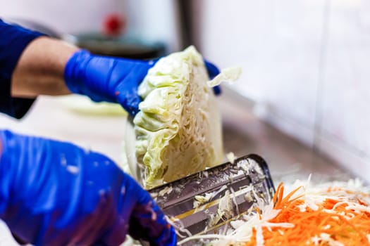hands in blue gloves cutting cabbage with special double blade slit cabbage shredder knife during sauerkraut preparation
