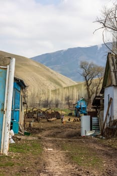 Poor rustic backyard with old blue tractor with dirt road between houses behind rusted steel gate at sunny spring day