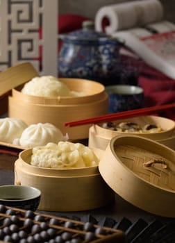 Chinese steamed pork shumai,  steamed pork bun, sweet bun and dampling in bamboo steamer with red chopstick on table. Traditional Chinese dim sum food.