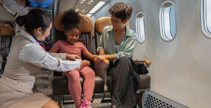 Air hostess helping a kid to fasten her seat belt. Happy family with little girl sitting at airplane. Airline transportation and travel concept.
