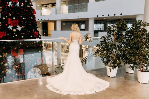 A beautiful and radiant bride poses gracefully in a stunning wedding gown in front of a festive Christmas tree