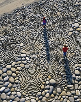 A photo-realistic image of an intricately arranged spiral pattern made from stones and pebbles on a sandy beach. The design stretches elegantly across the sand, capturing the serene and creative beauty of nature and human artistry.