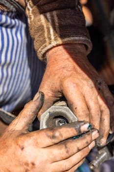 Dirty and calloused hands of a mechanic assembling compressed coil spring during DIY car repairs. Closeup.