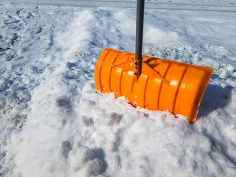 An orange snow shovel sticks out of a snowdrift a sunny winter morning