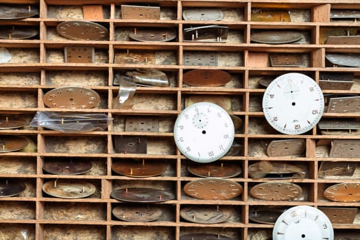 compartmentalized tray holds various watch dials in individual slots, organized systematically for easy access, reflecting the efficient storage needs of a well-used watch repair shop