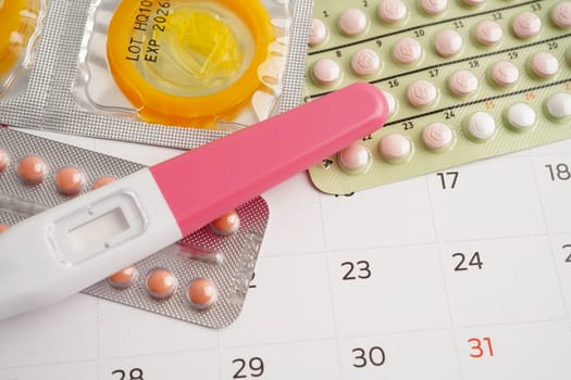 Pregnancy test with birth control pills and condom for female on calendar, ovulation day.