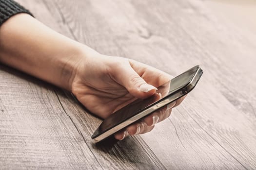 smartphone is gently held by a light-skinned hand with well-maintained, glossy nails. Background blur accentuates the phone and hand, suggesting focus on connectivity and calmness