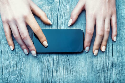smartphone lies on a wooden surface, bordered by two hands with light skin and manicured nails. The images soft lighting and textured background suggest minimalism and calm
