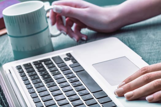 Light-skinned hand with polished nails gently pressing a laptop key. A blurred coffee cup in the background creates a calm workspace, focusing on precision and productivity
