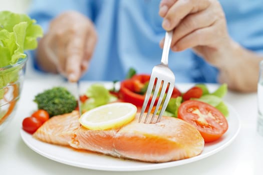 Asian elderly woman patient eating salmon stake and vegetable salad for healthy food in hospital.