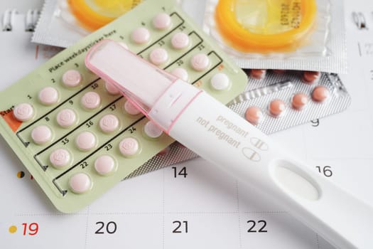 Pregnancy test with birth control pills and condom for female on calendar, ovulation day.