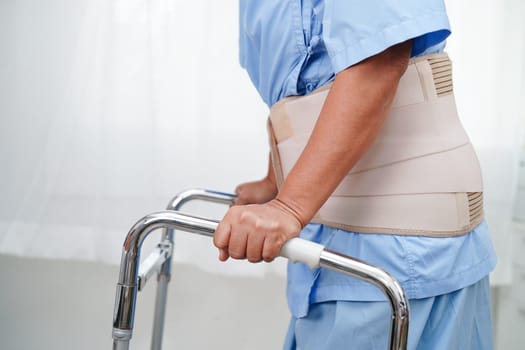 Asian senior pain back wearing elastic support belt with walker.