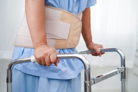 Asian senior pain back wearing elastic support belt with walker.