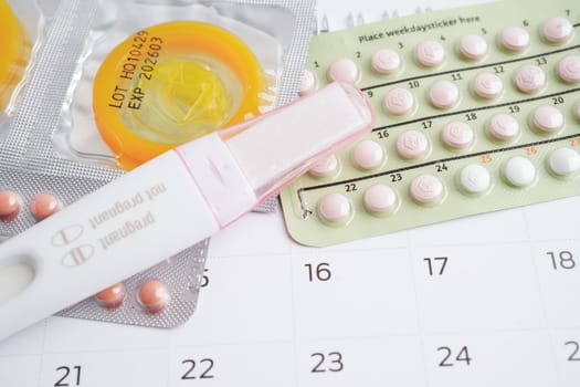 Pregnancy test with birth control pills and condom for female on calendar, ovulation day.