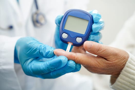 Asian doctor using digital glucose meter for check sample blood sugar level to treatment diabetes.