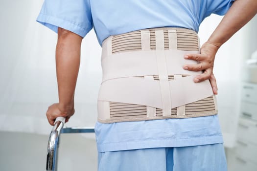 Asian senior pain back wearing elastic support belt with walker.