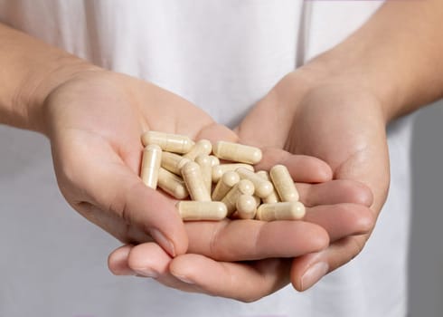 Cupped female hands with a pile of beige medical capsules closeup over white shirt. Alternative herbal products for health care